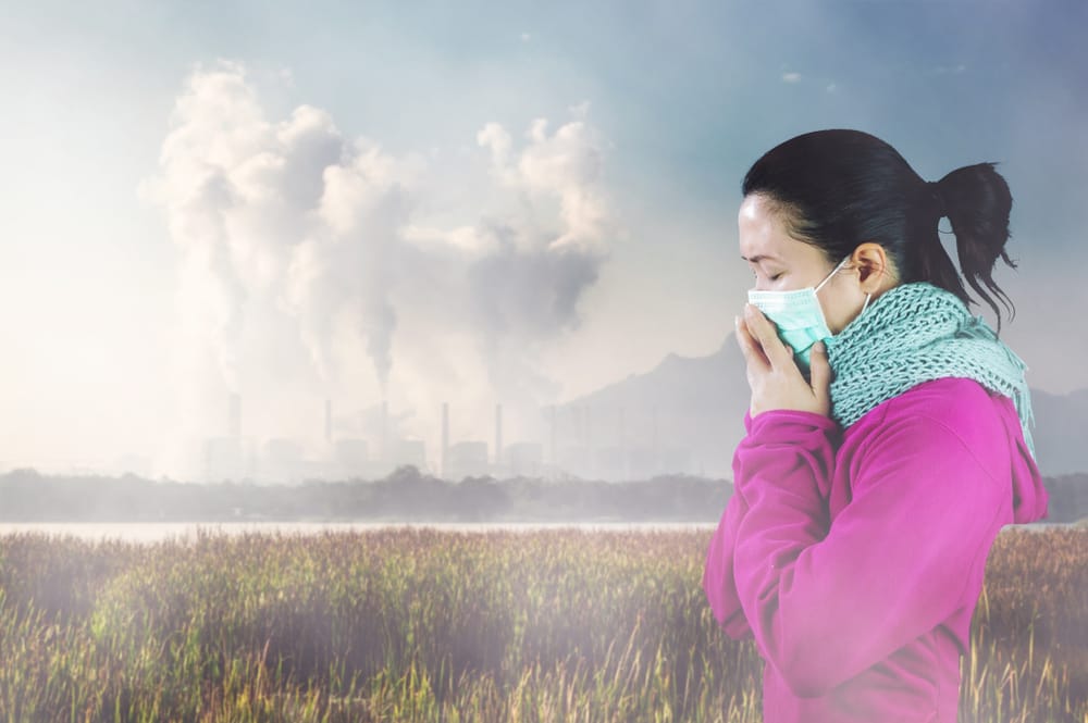 woman holding mask to face with polluting factory in background