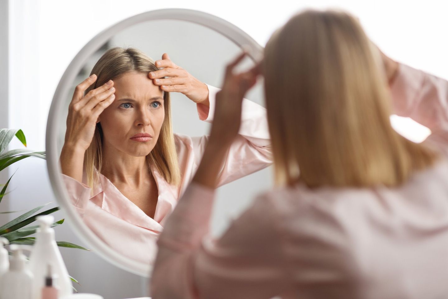 middle aged woman looking at forehead wrinkles in mirror
