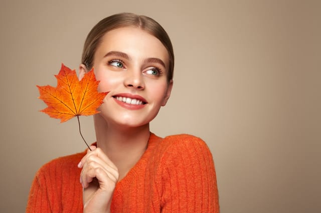 Portrait of beautiful young woman in orange blouse with autumn leafs. Healthy clean fresh skin natural make up beauty eyes