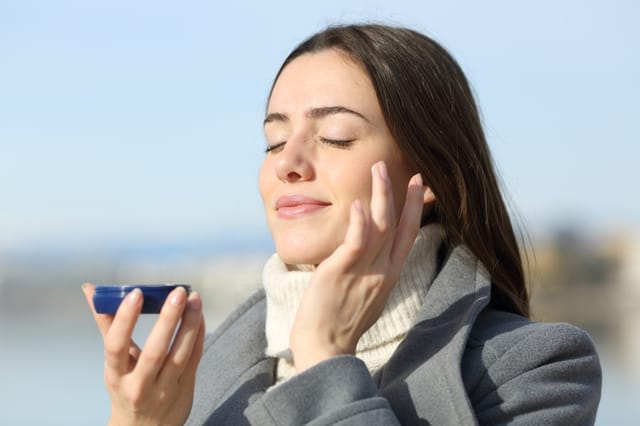 Satisfied woman in winter applying moisturizing cream on cheek