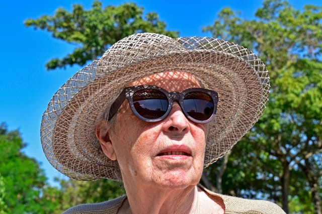 Senior old woman with sun hat and sun glasses pondering age skin sun damage possible