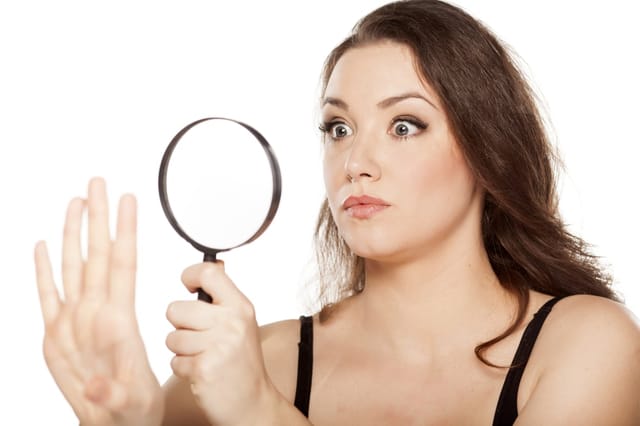 astonished young woman looking at her nails with a magnifying glass